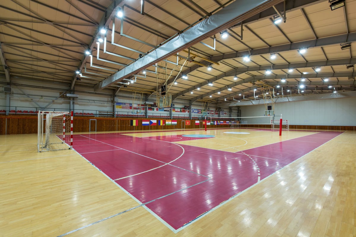 Bright empty indoor gymnasium featuring volleyball net and basketball backboards